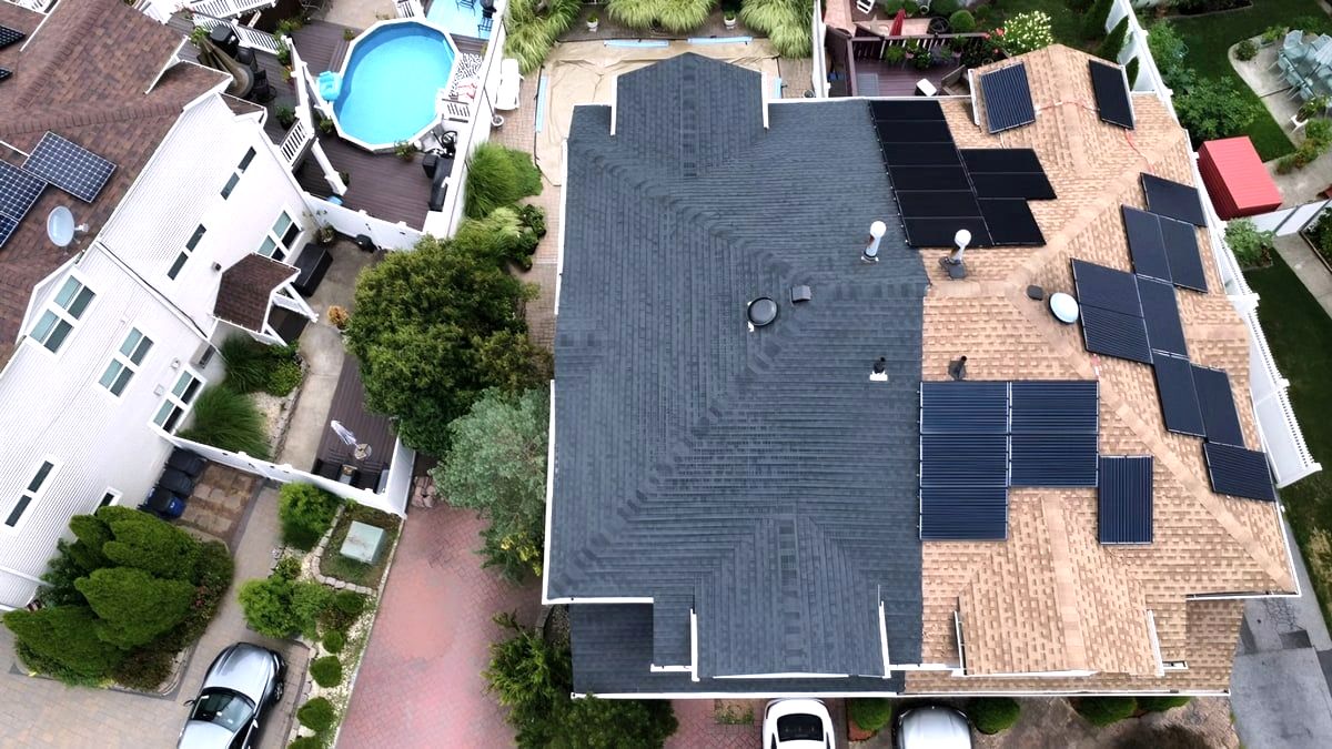 Aerial of house roof, half new dark shingles, half old with solar panels